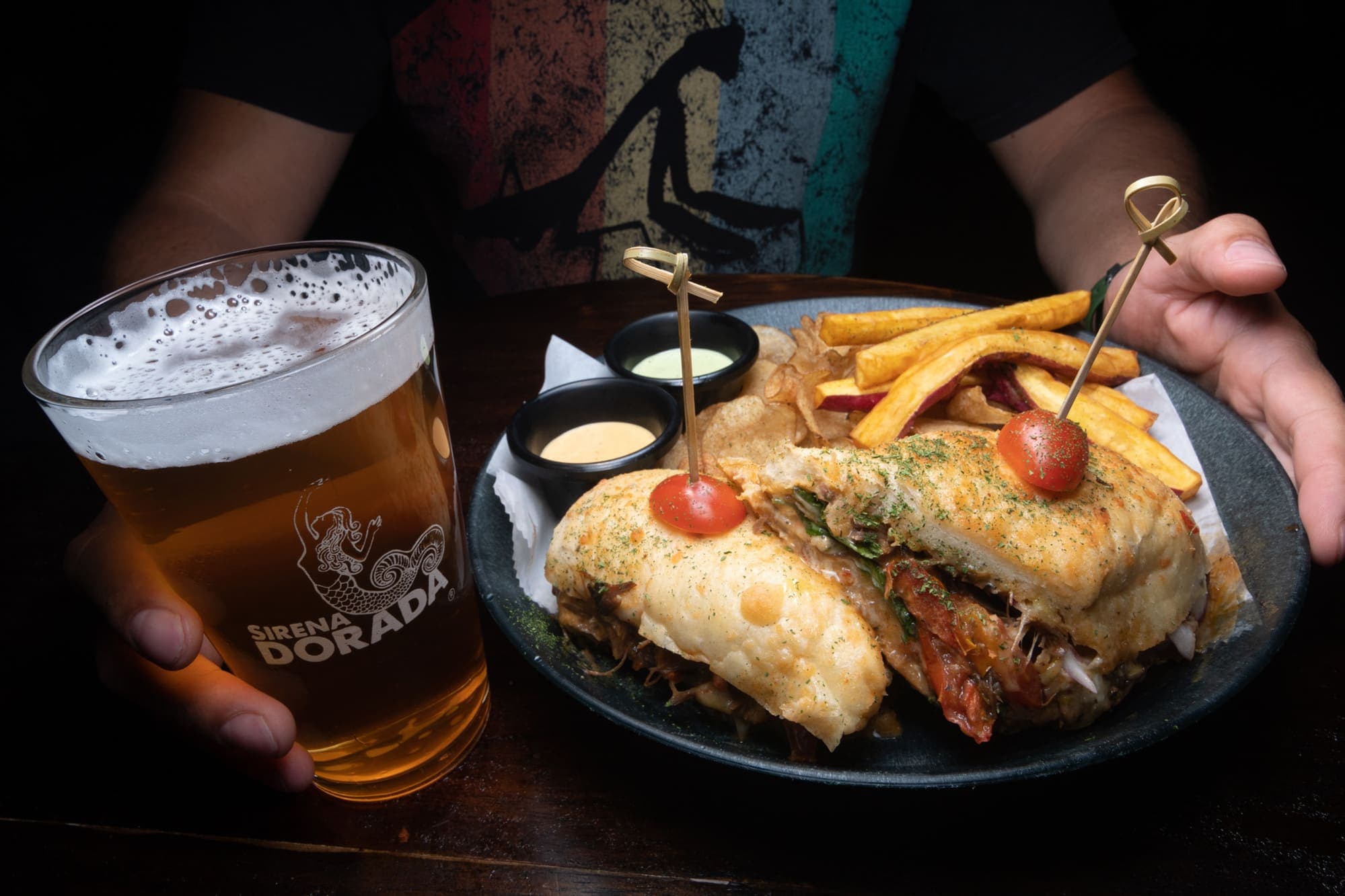 Un sándwich con papas y una pinta de cerveza dorada al lado