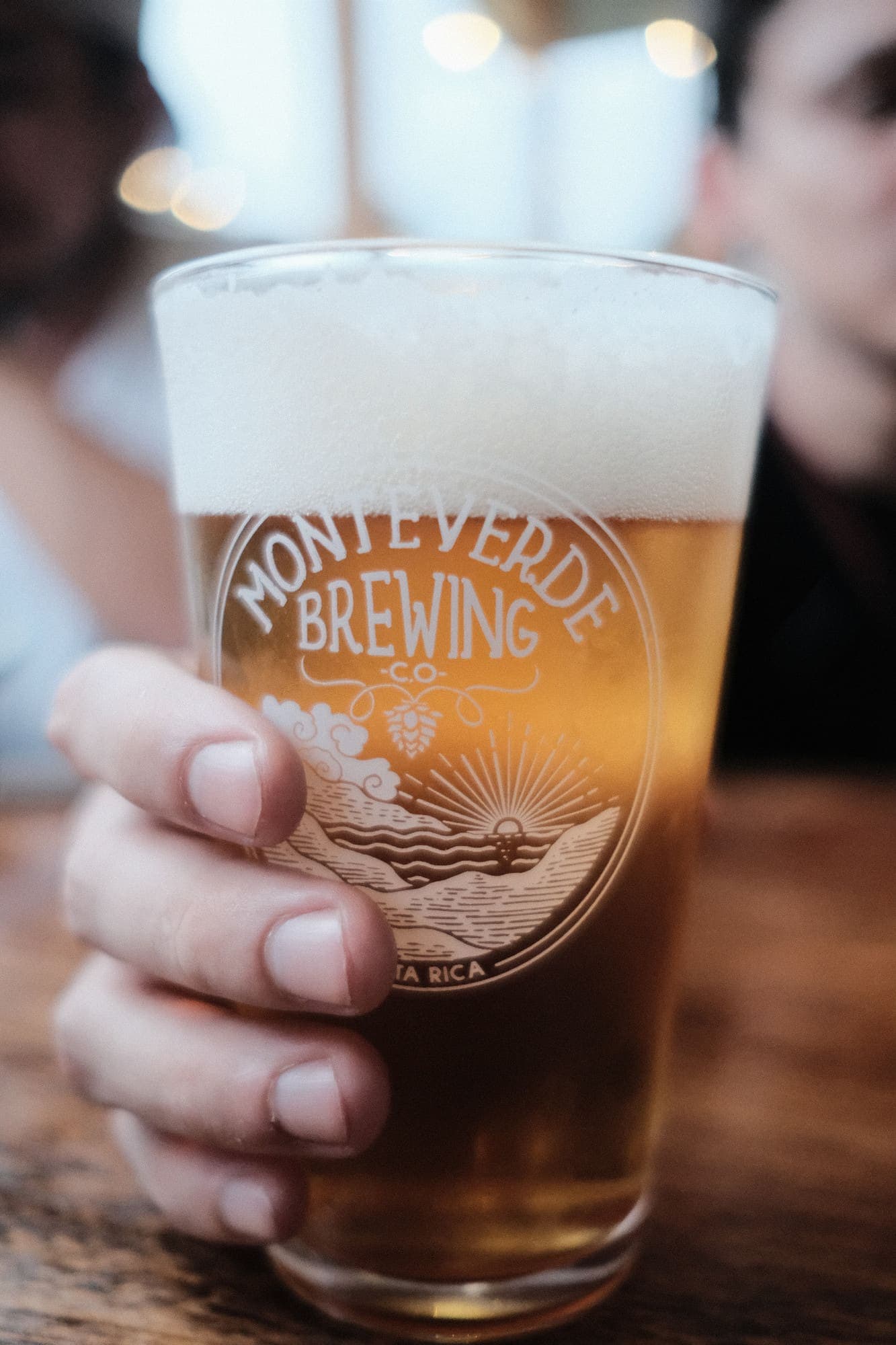 Una pinta de cerveza dorada de Monteverde Brewing Company a contraluz frente al bosque